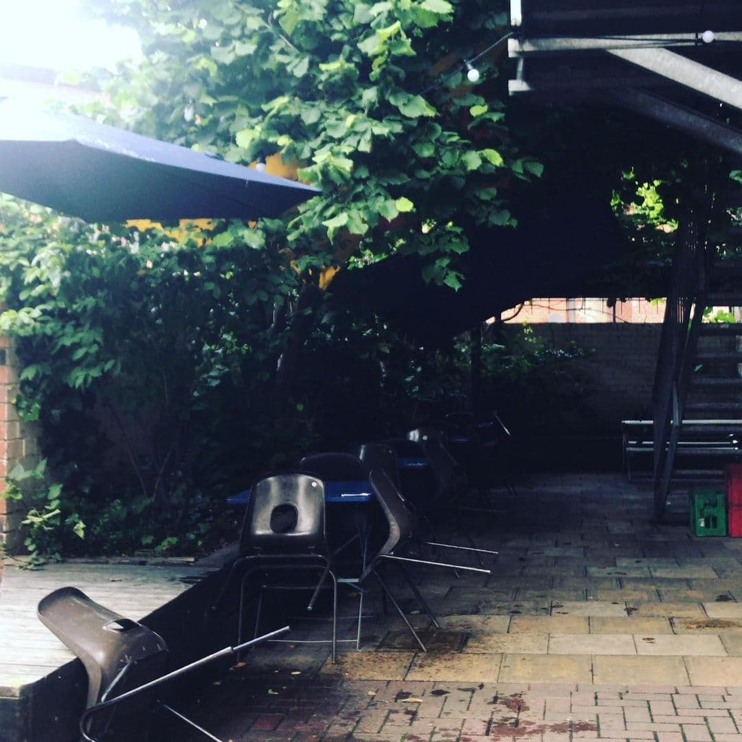 Outdoor seating area with black chairs under a canopy surrounded by lush greenery at Wharf Chambers.