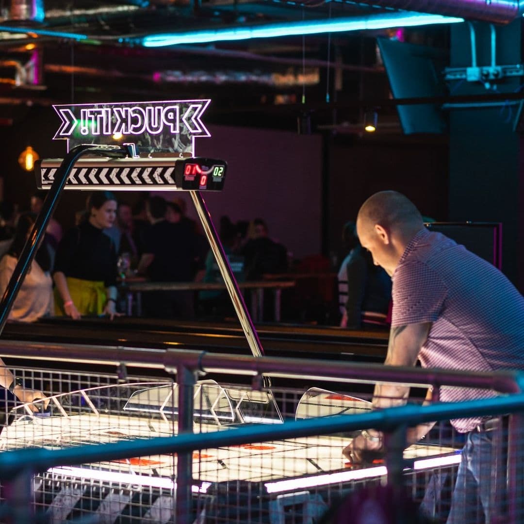 Patron playing air hockey at Boom Battle Bar with neon lighting and other guests in the background.