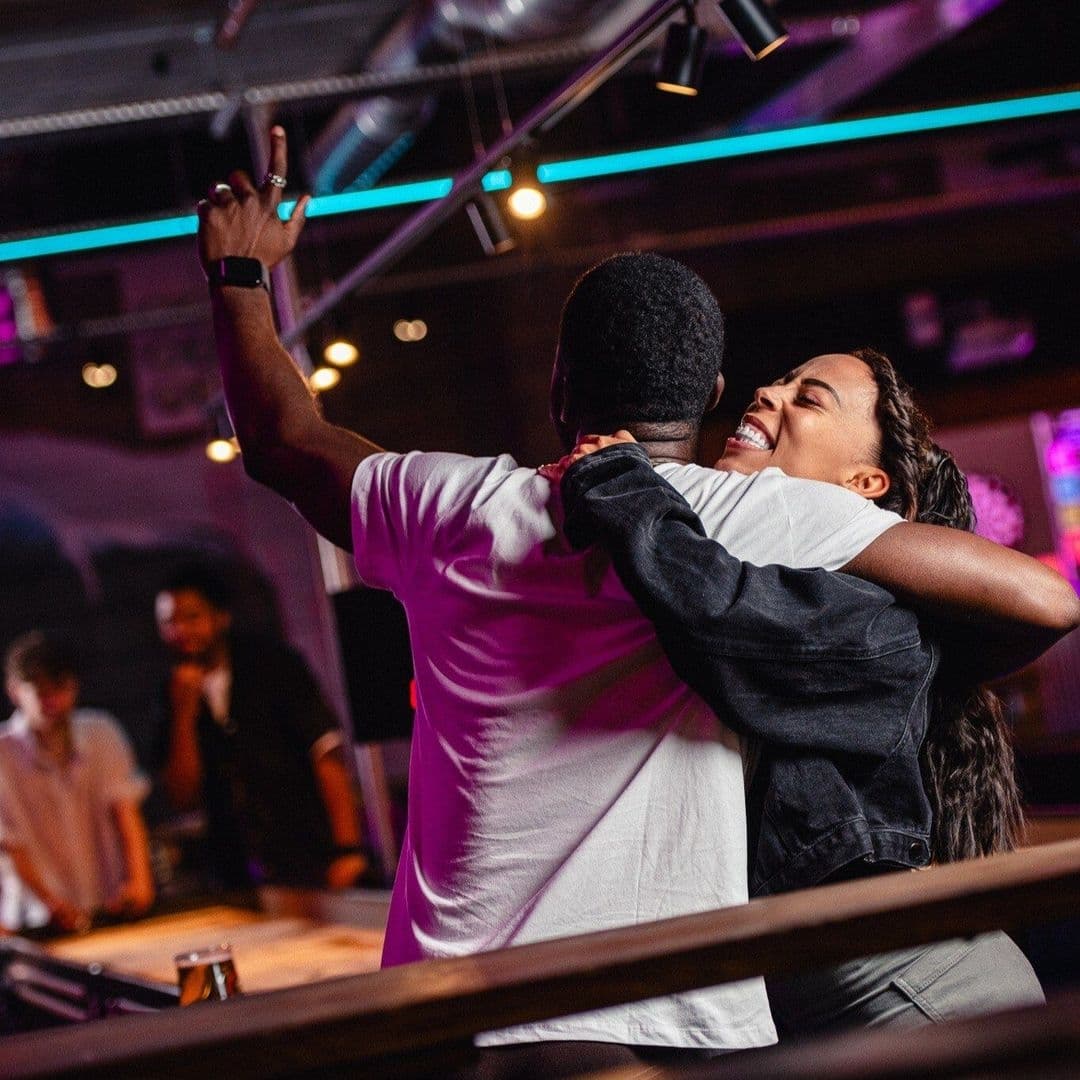 Visitors enjoying a lively moment at Boom Battle Bar, with a man and woman embracing and celebrating, surrounded by a vibrant atmosphere with neon lights.