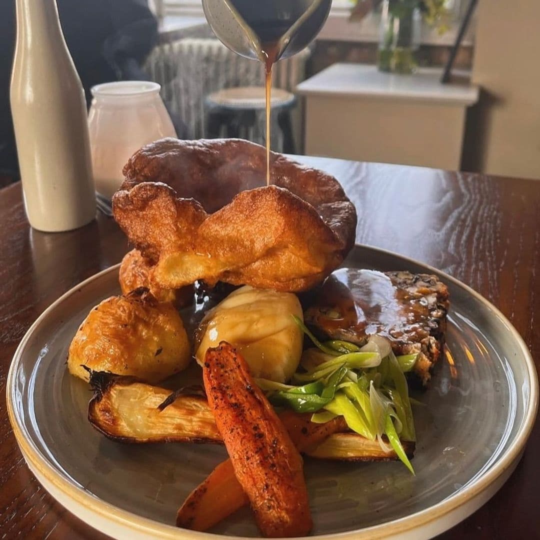 Traditional Sunday roast dinner served at Lamb And Flag, featuring a large Yorkshire pudding, roasted vegetables, and gravy being poured over the dish.