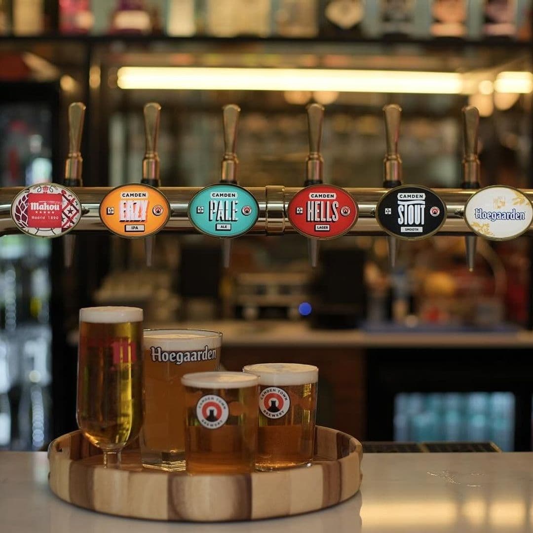 Variety of draft beers on tap at OHANA bar with a wooden tray holding a Hoegaarden glass and two pints of beer in the foreground.