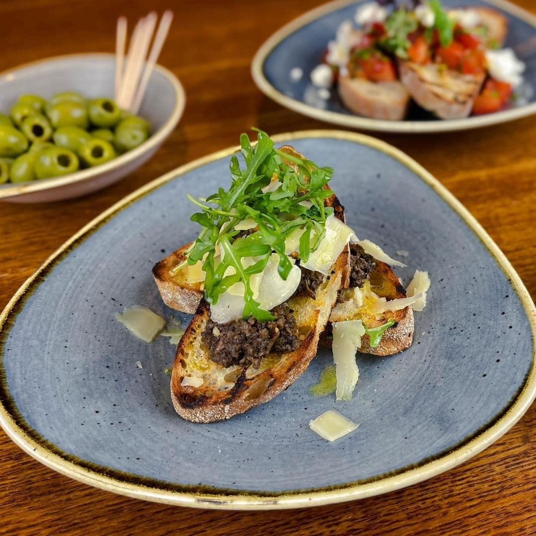 Gourmet bruschetta with minced meat, cheese shavings, and fresh arugula on a blue ceramic plate at Scotts Arms.