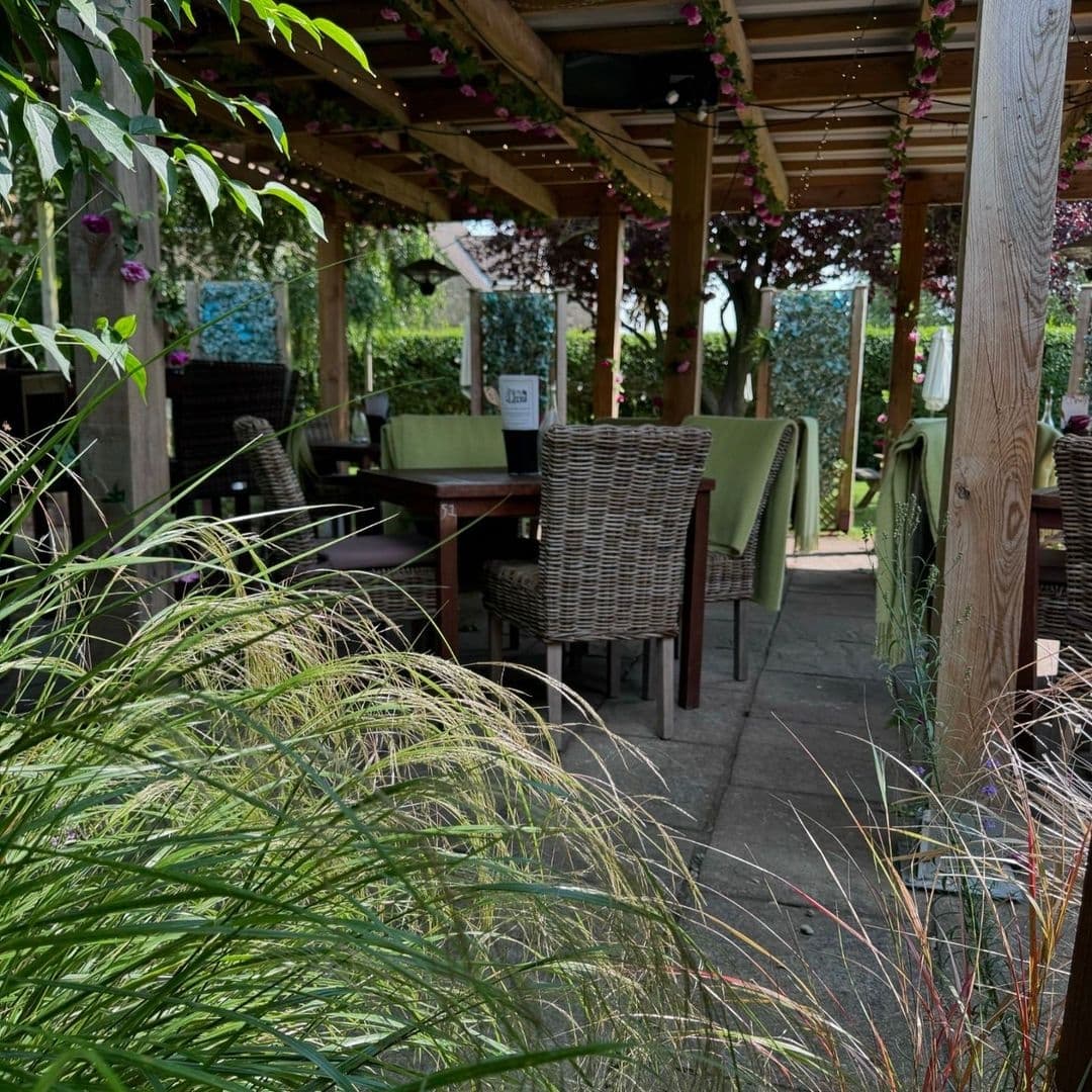 Outdoor seating area at Scotts Arms with wicker chairs, wooden tables, and a pergola adorned with flowering plants.