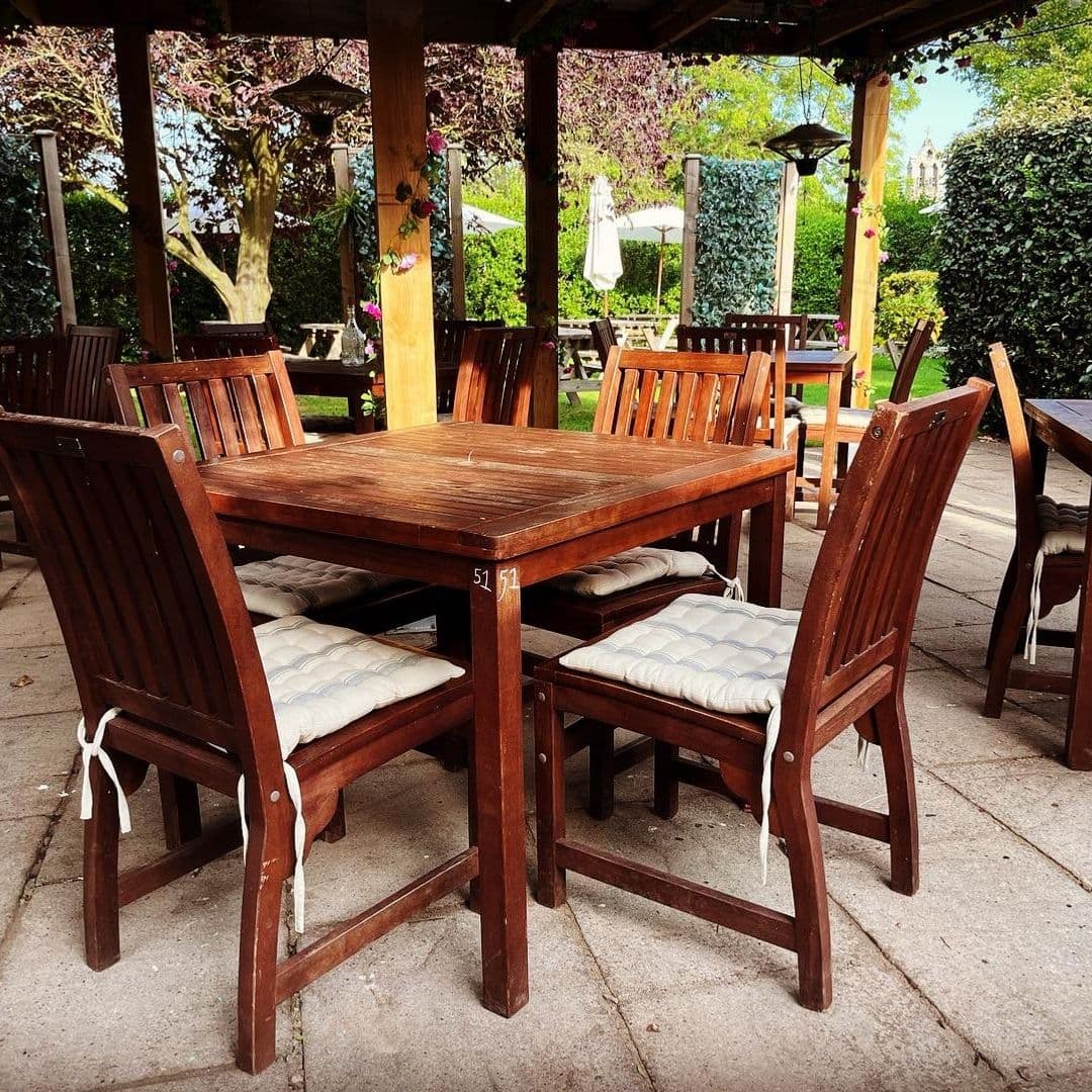Outdoor dining area at Scotts Arms with wooden tables and chairs under a pergola, surrounded by greenery.
