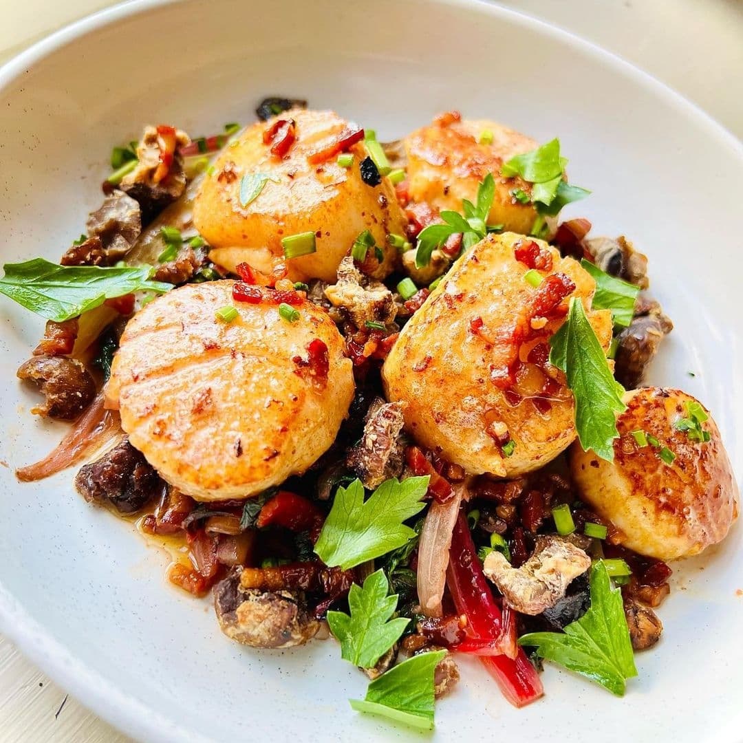 Pan-seared scallops with garnishes served on a white plate at The Chequers Inn.