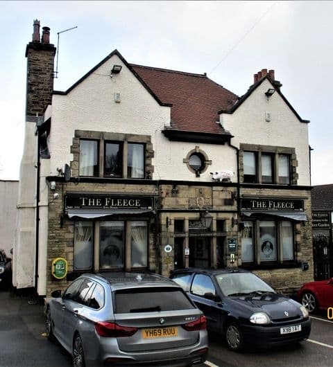 Exterior view of The Fleece, a traditional two-story building with a white and black facade, featuring large windows with signage, flanked by parked cars.