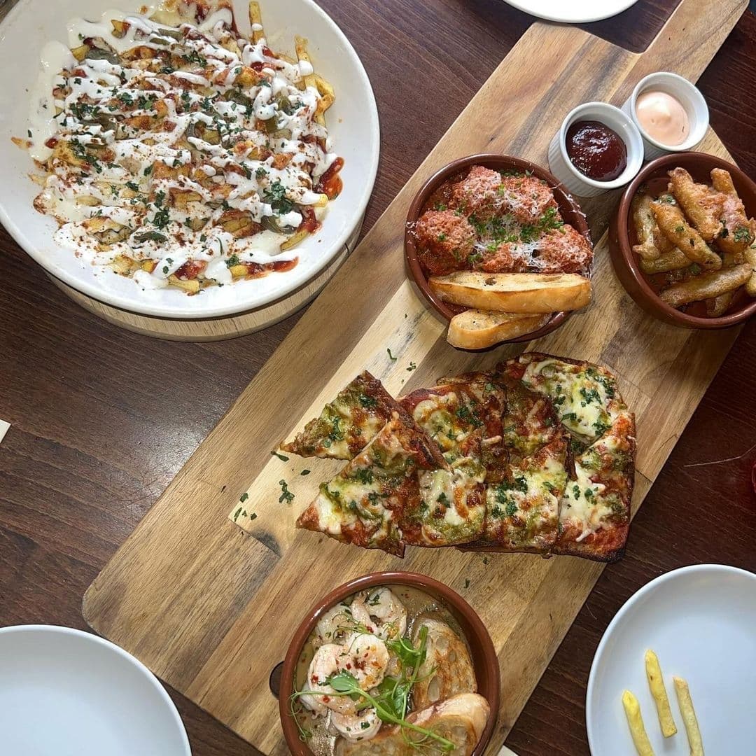 Assorted gourmet dishes at The Thornhill featuring loaded fries, meatball marinara, garlic bread, and shrimp cocktail served on a wooden table.