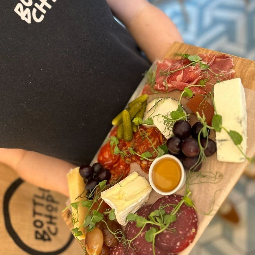 Server presenting a charcuterie board with assorted cheeses, cured meats, pickles, and grapes at Bottle Chop.