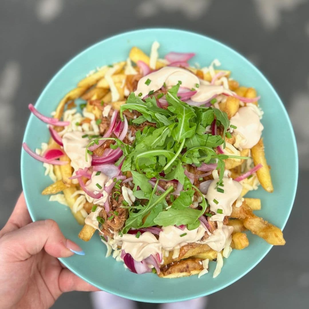Plate of gourmet fries topped with pulled pork, red onions, arugula, and creamy sauce served at Cup 19 Coffee.