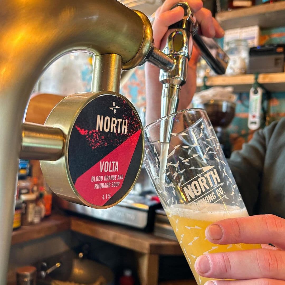 Pouring a craft beer from a tap at Doghouse Bar & Bagel Shop, featuring a close-up of the beer tap with the North Brewing Co. logo and a glass being filled.
