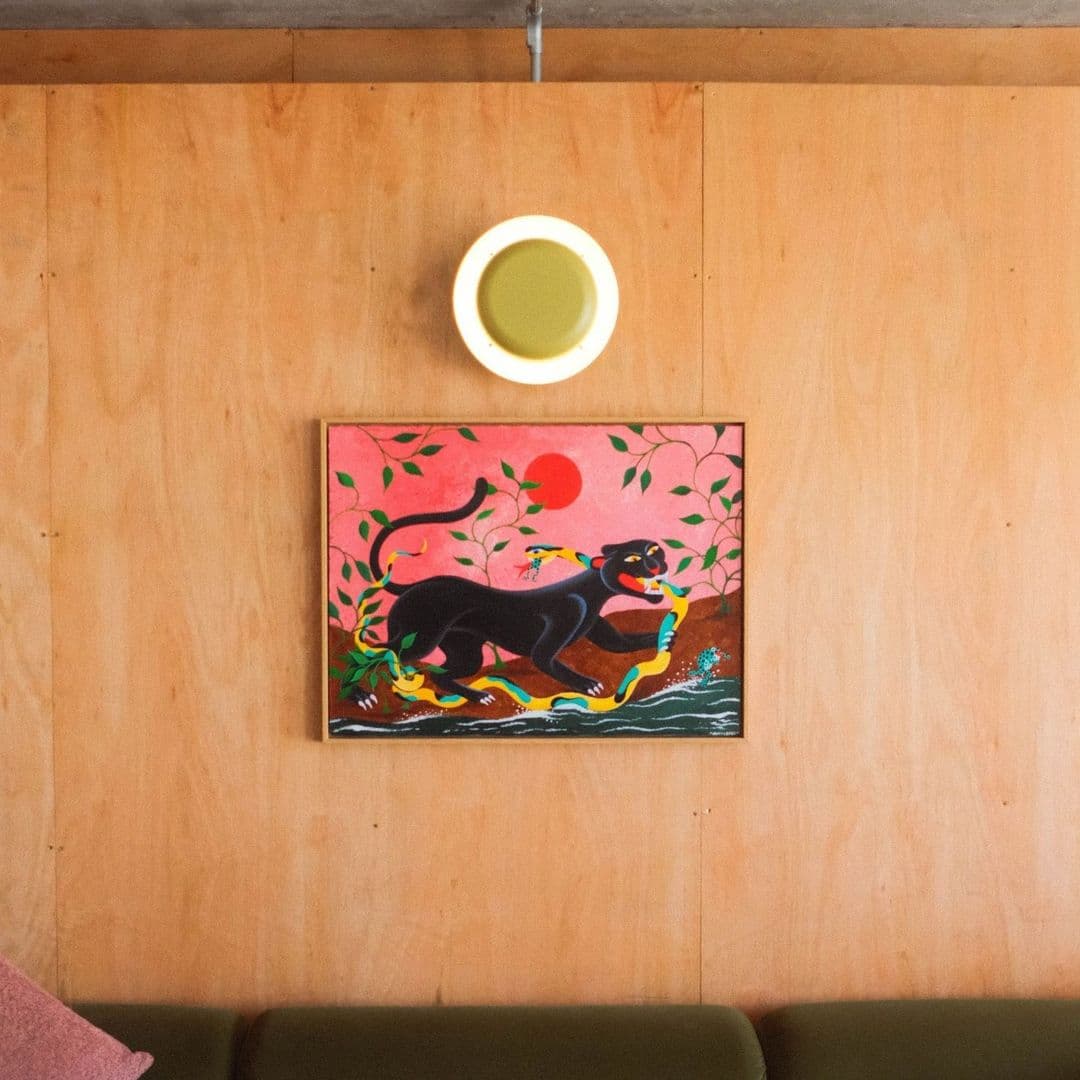 Colorful painting of a black panther in a vibrant landscape on the wall at Galleria, with a simple round light fixture above it.