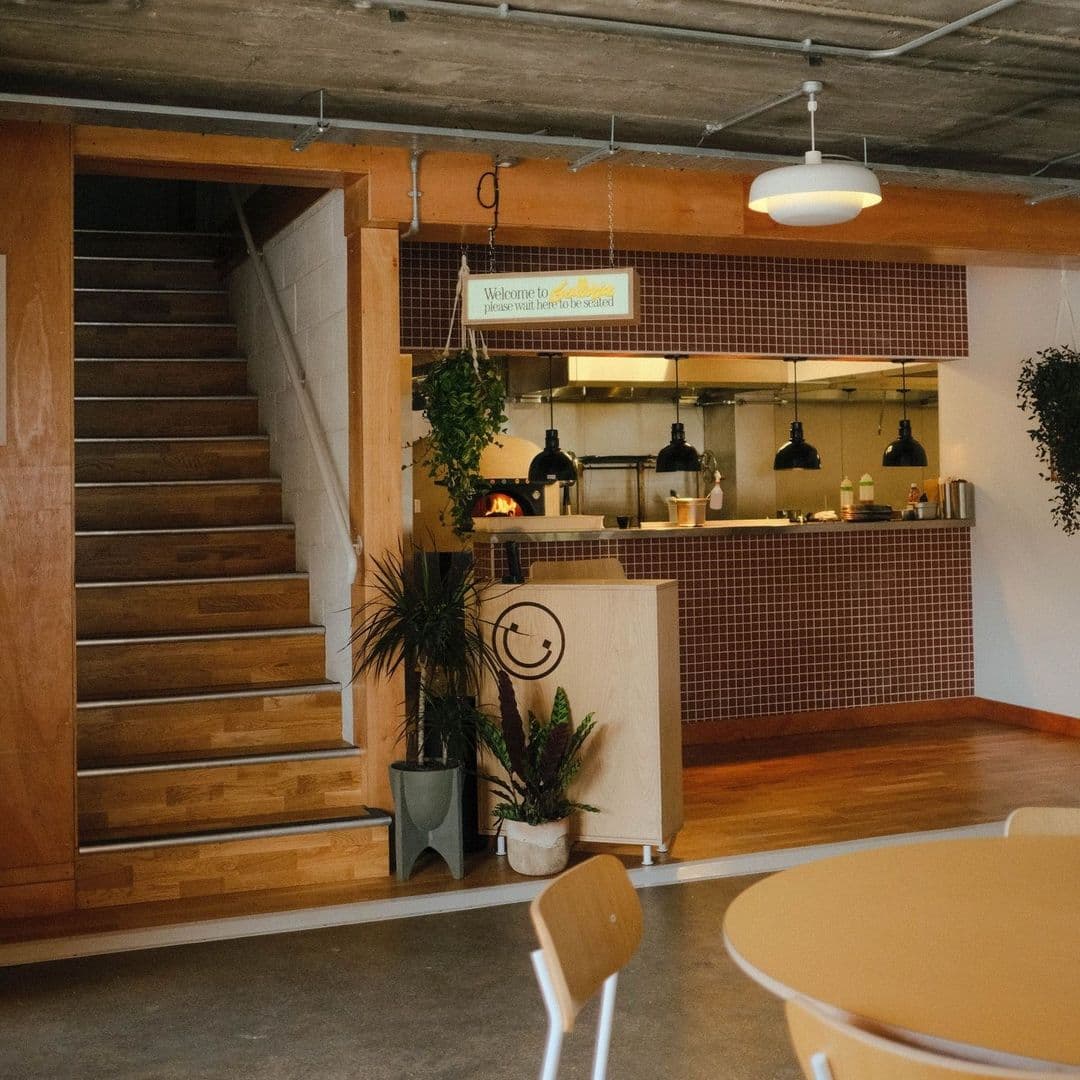 Interior of Galleria featuring a cozy café corner with wooden stairs, a welcoming sign, pendant lights, and green potted plants.