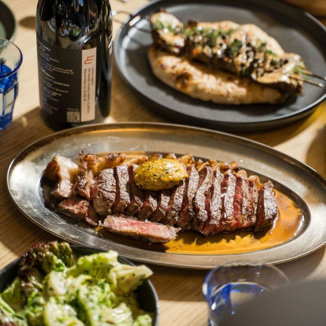 Sliced steak with herb butter on a plate, grilled chicken, and salad served at Galleria's dining experience.