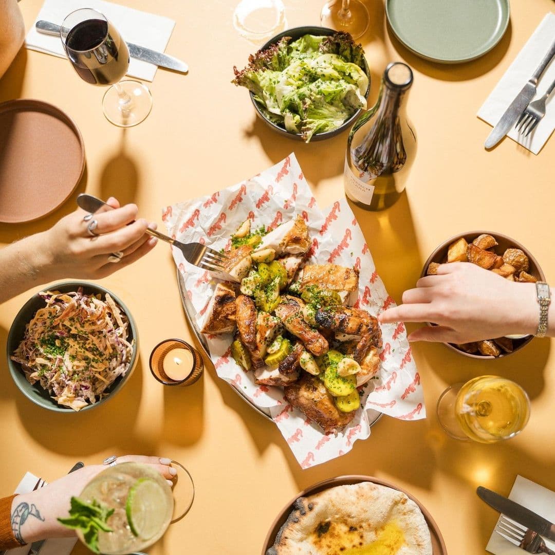 Overhead view of a dining experience at Galleria featuring a variety of dishes, including grilled chicken, salad, roasted potatoes, and flatbread, with diners enjoying wine and cocktails.