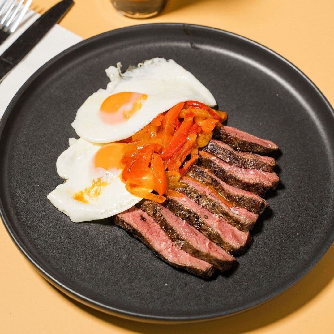 Sliced steak with fried eggs and grilled peppers served on a black plate at Galleria.