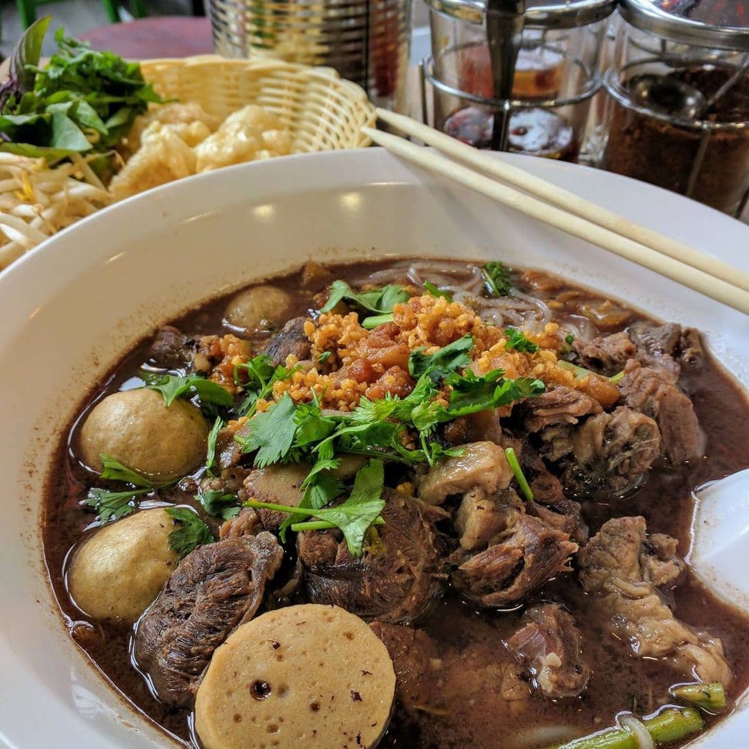 A bowl of traditional Thai noodle soup with beef, meatballs, and fresh herbs at Little Mommy Thai.