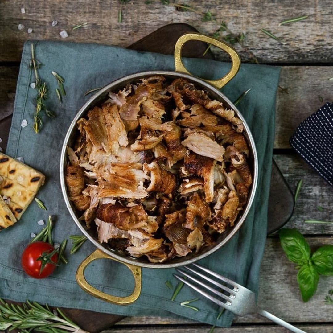 Aromatic shredded meat served in a metal pan at Santorini Bar and Grill, with fresh herbs, a tomato, and crackers on a rustic wooden table.