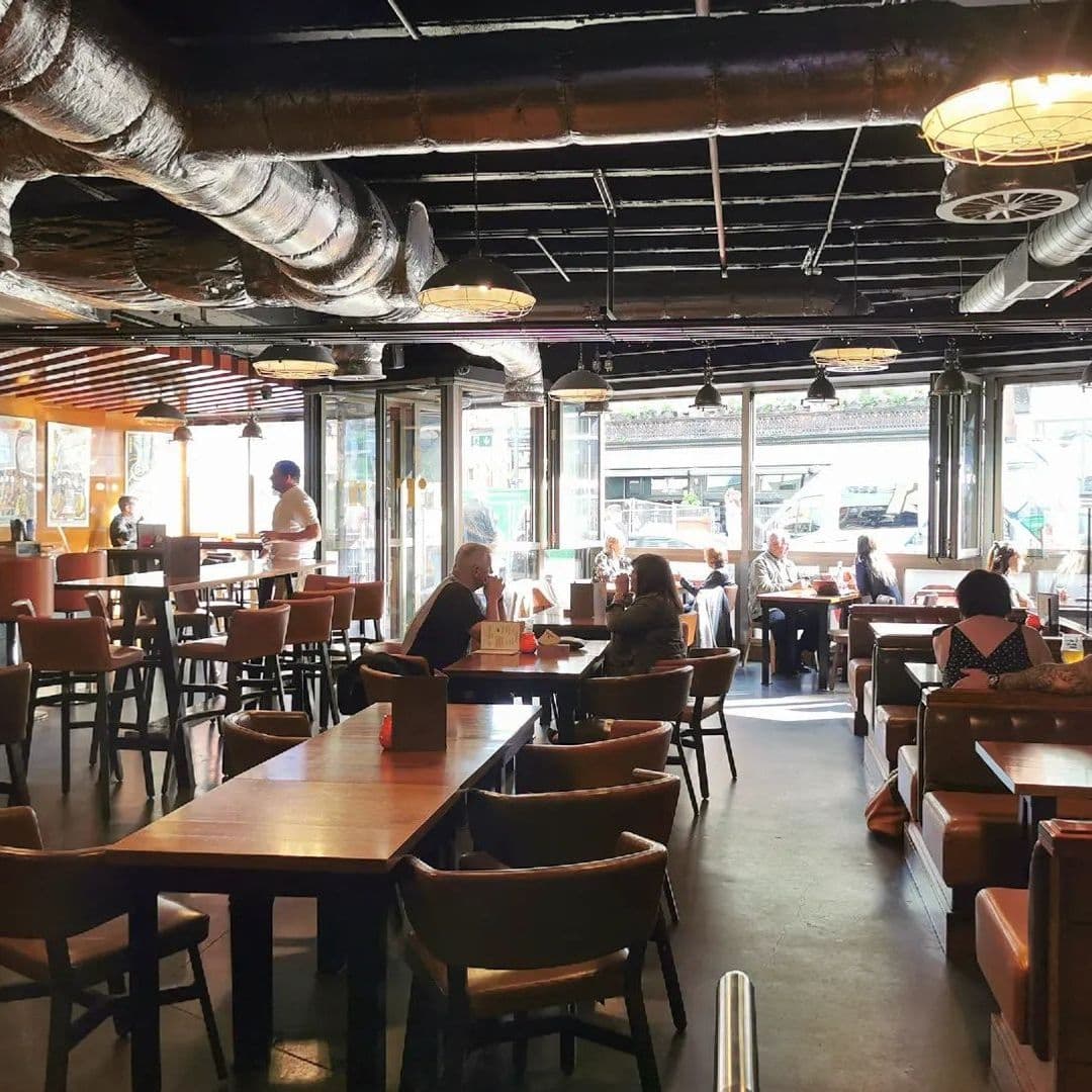 Interior of Tapped, featuring a casual dining area with wooden tables and chairs, patrons enjoying their time, and large windows allowing natural light to fill the space.