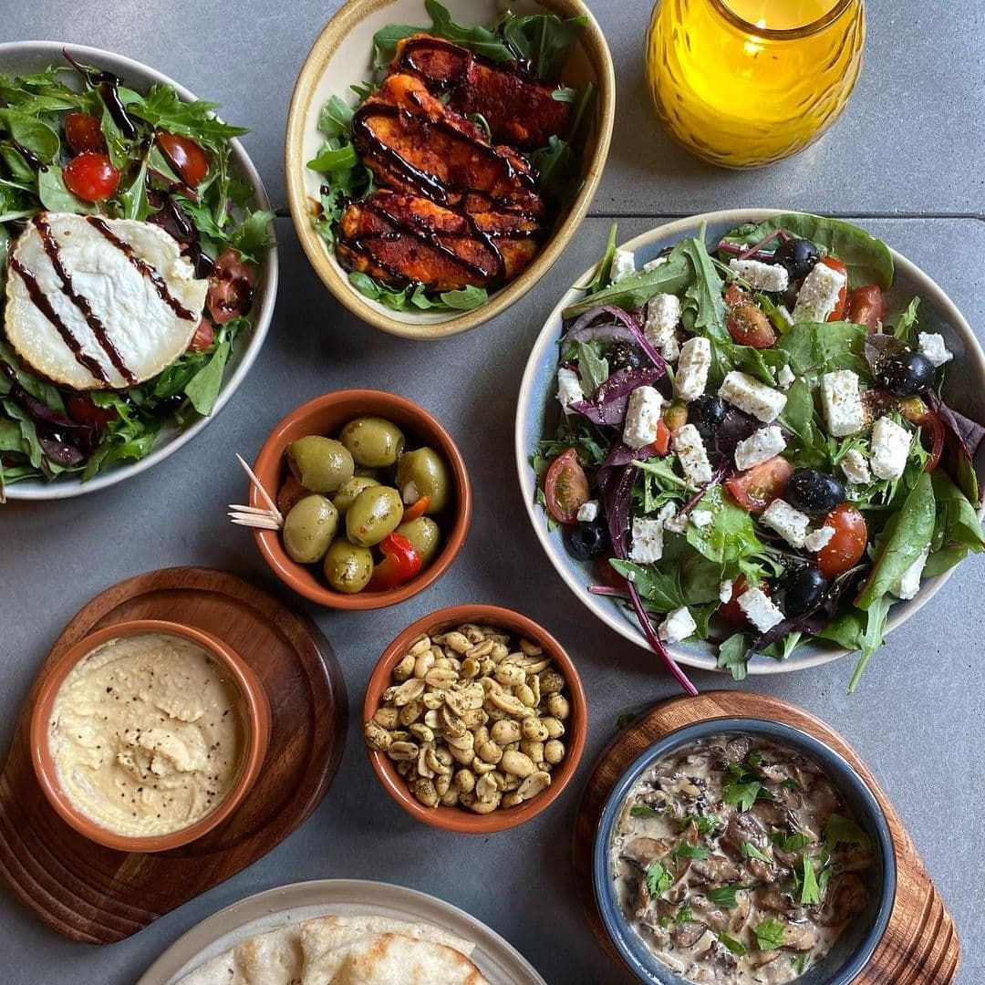 Assorted Mediterranean dishes at Tapped, featuring salads with feta cheese, grilled vegetables, hummus, olives, pita bread, and seasoned nuts.