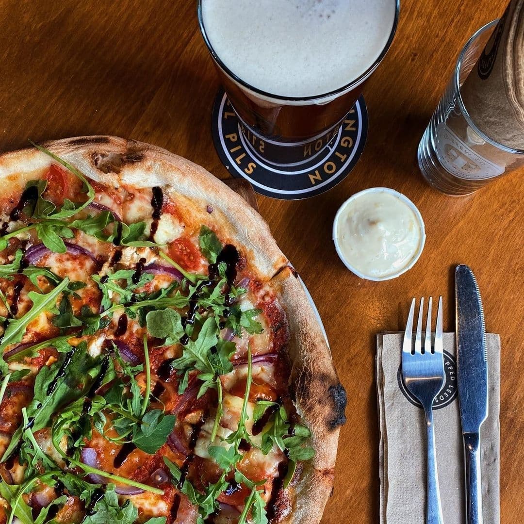 Gourmet pizza with arugula topping and a pint of beer at Tapped restaurant.