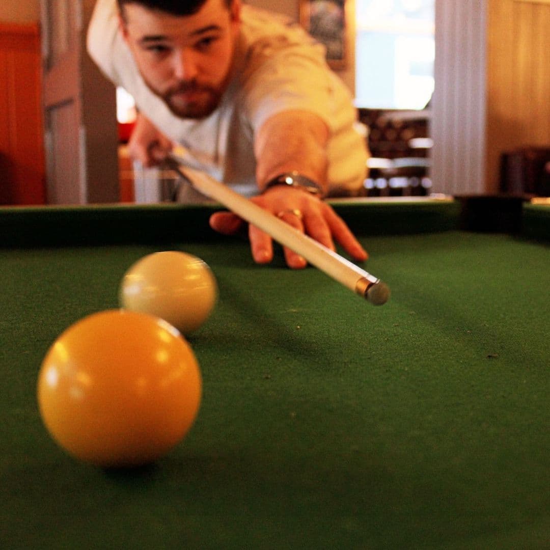 "Man playing pool at The Eldon Pub, focusing on a shot with cue stick and billiard balls on green felt table."