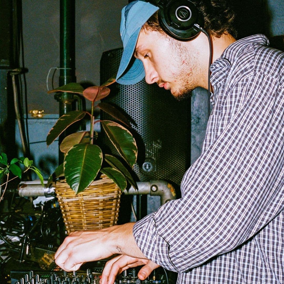 DJ performing at The Old Red Bus Station with headphones and mixing equipment.