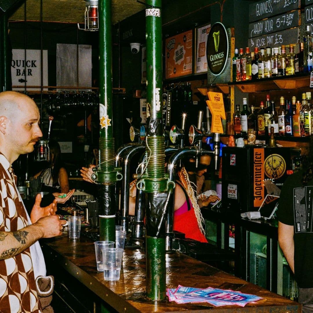 Patrons at the bar inside The Old Red Bus Station, featuring beer taps, a variety of spirits, and a vibrant atmosphere.
