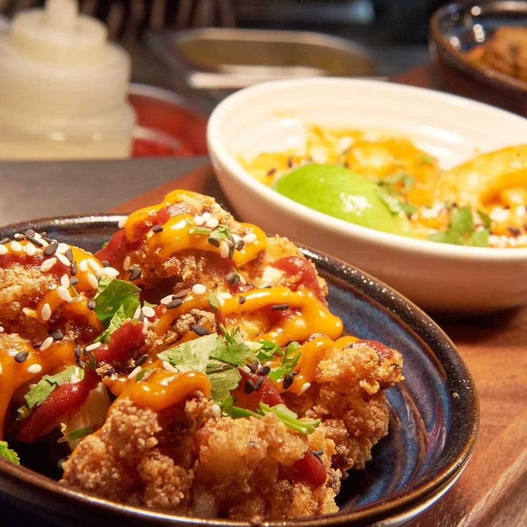 Appetizing plate of crispy fried chicken topped with sesame seeds, herbs, and drizzles of tangy sauces at Hesco Lounge.