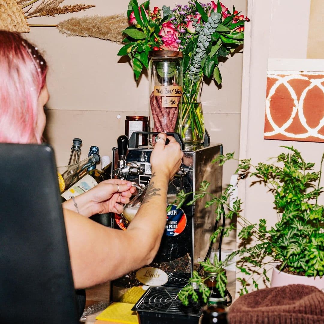 Person preparing a drink at Hoc Loco's cozy bar with fresh flowers and assorted bottles in the background.