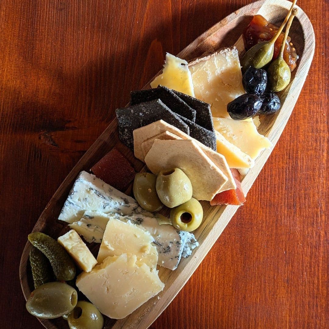 Assorted cheese platter with olives, pickles, and crackers on a wooden board at Hoc Loco.