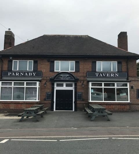 Exterior view of Parnaby Tavern, featuring a traditional brick building with black awnings, large windows, and a central entrance flanked by wooden benches.