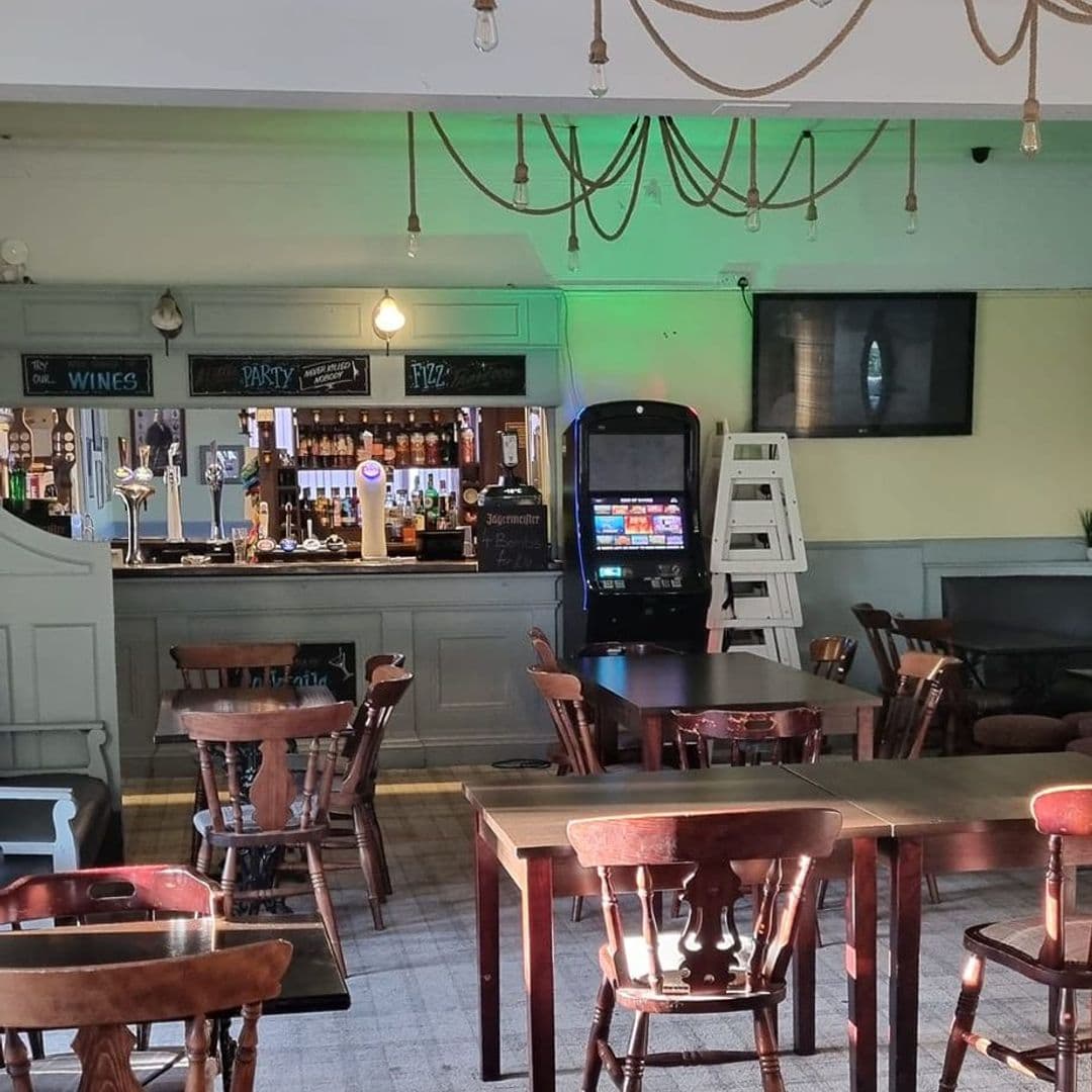 Interior of Parnaby Tavern showing wooden tables and chairs, a bar with various bottles and taps, a fruit machine, and a television on the wall.