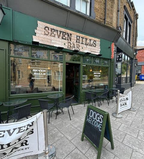 Exterior view of Seven Hills Bar with outdoor seating, a welcoming sign for dogs, and visible entrance.