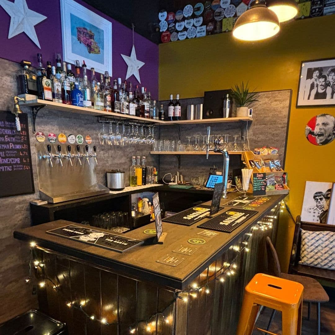 Cozy bar interior at Seven Hills with a selection of beers on tap, shelves stocked with various bottles, and colorful wall decor featuring stars and artwork.