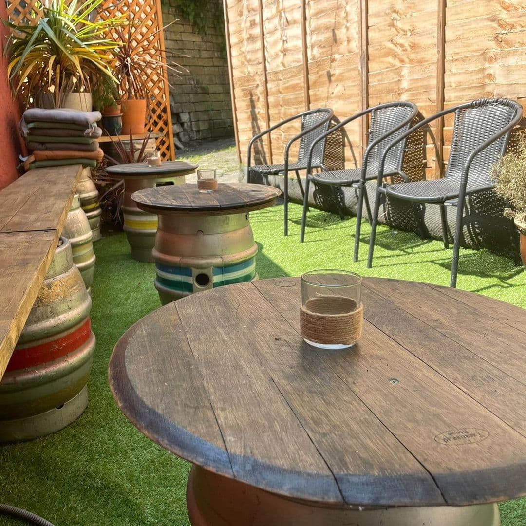 Cozy outdoor seating area at Seven Hills with wooden tables, wicker chairs, and decorative plants on artificial grass.