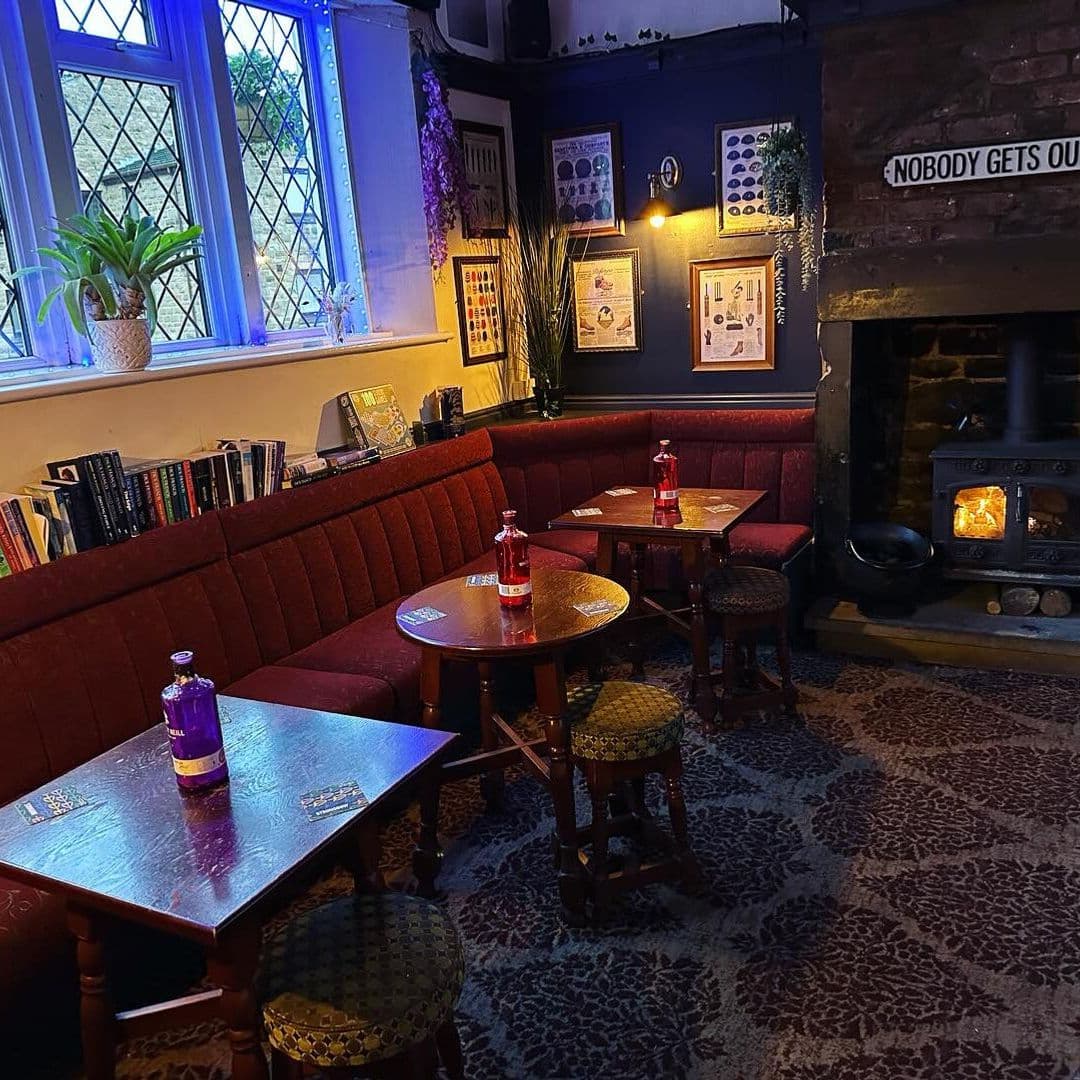 Cozy interior of The Commercial with red upholstered bench seating, small wooden tables, stools, a lit fireplace, and framed artwork on blue walls.