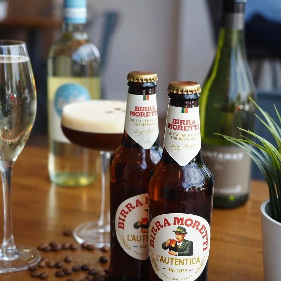 Alt text: A selection of drinks at Kofi&Co – Roundhay, featuring two bottles of Birra Moretti, a cocktail with frothy top, a glass of sparkling wine, and a bottle of white wine, with coffee beans scattered on the table.