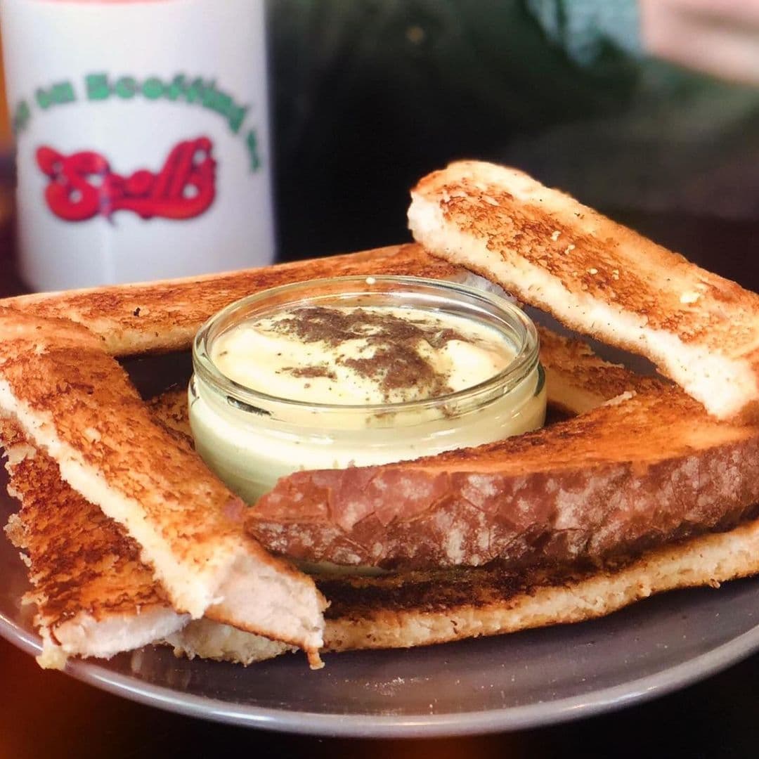 Delicious toast served on a plate with a small jar of creamy dip in the center. The toast is golden brown and crispy, showcasing a warm and inviting meal at Scoffs Feel Good Food.