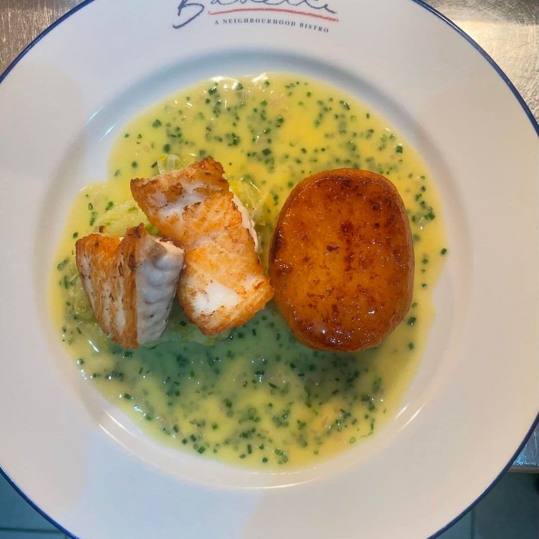 Delicious dish served at Bavette Bistro featuring golden-brown fish fillets, a round fried potato, and a creamy green sauce with herbs. The meal is presented on a white plate with the bistro's logo.