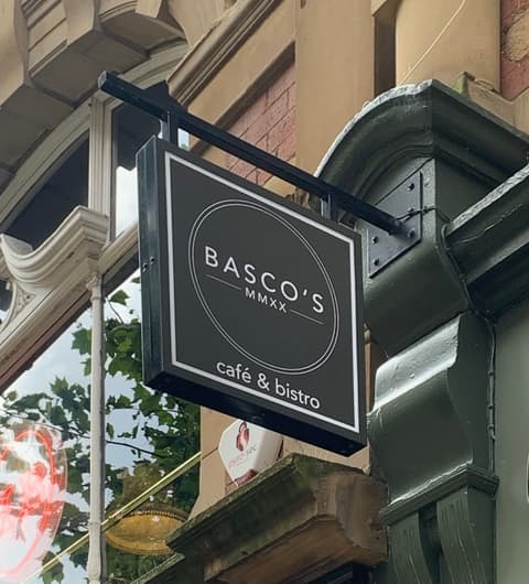 Black and white sign for BASCO'S café & bistro hangs from a green awning, surrounded by historic brick architecture.