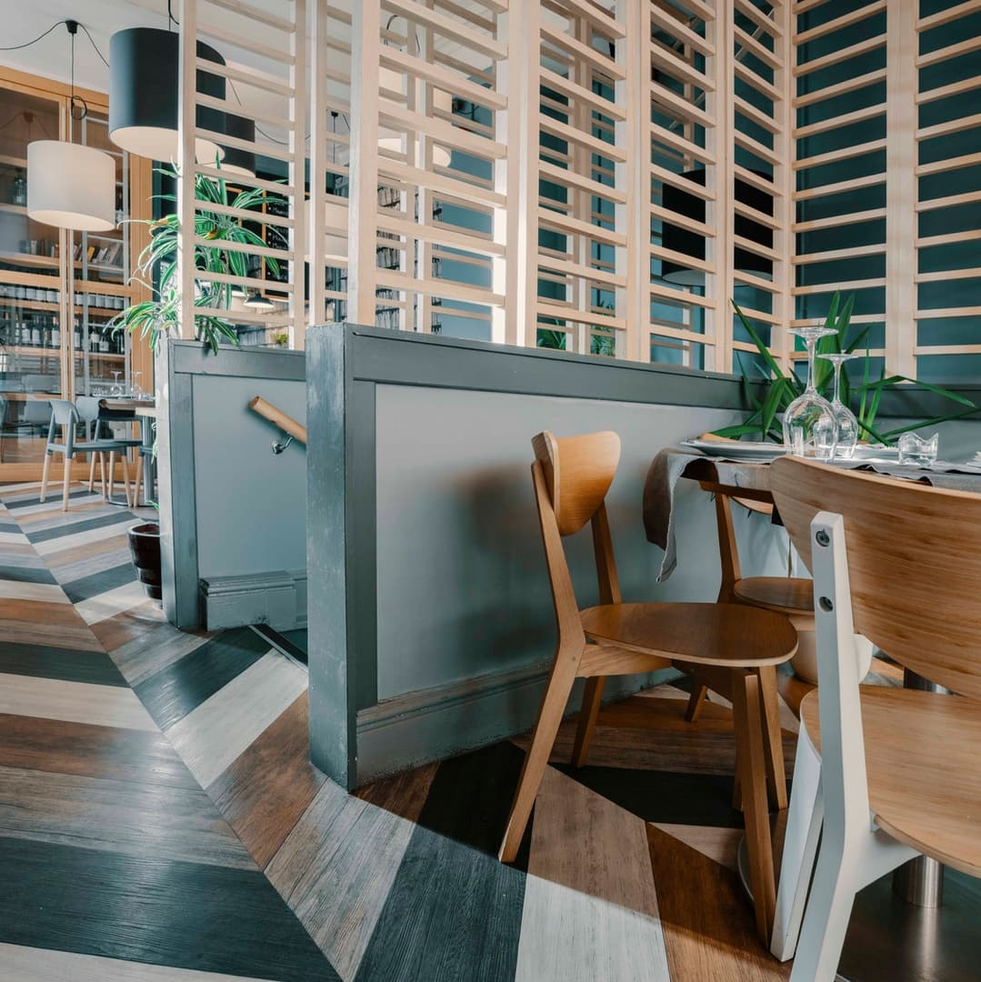 Modern cafe interior with wooden accents, geometric flooring, and plants, creating a warm and inviting atmosphere.