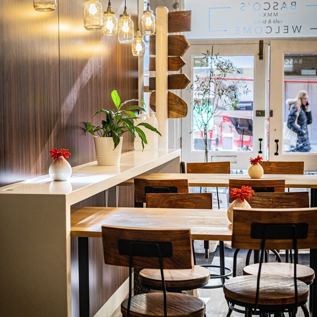 Cozy cafe interior with wooden tables, stylish chairs, hanging pendant lights, and a welcoming plant centerpiece.