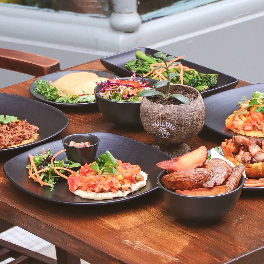 A vibrant spread of colorful dishes featuring tacos, salads, and roasted potatoes on a wooden table.
