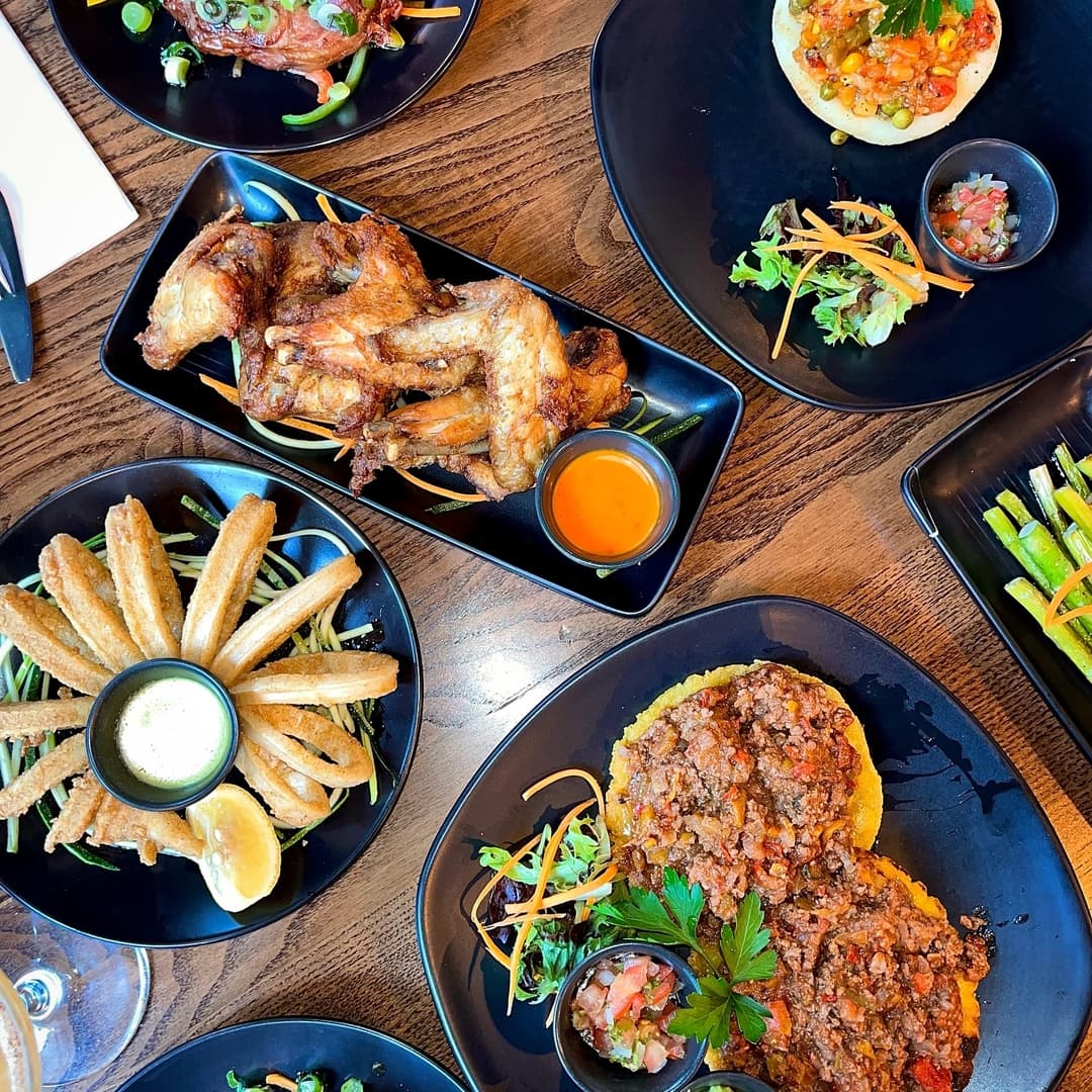 A vibrant spread of dishes at Casa Leeds, featuring wings, churros, tacos, and fresh garnishes on sleek black plates.