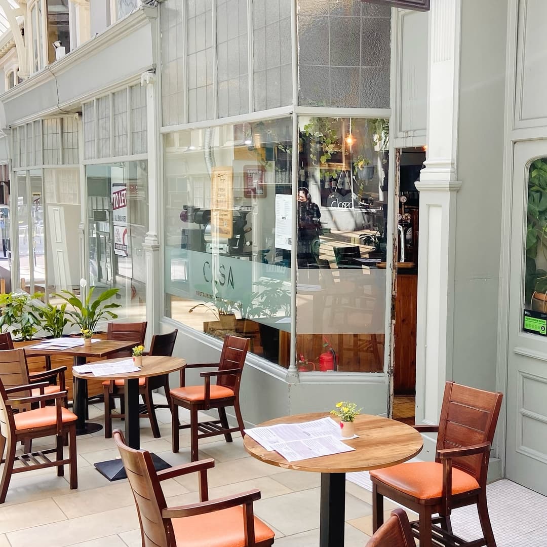 Charming café patio with wooden tables, chairs, and potted plants, inviting a cozy dining atmosphere.