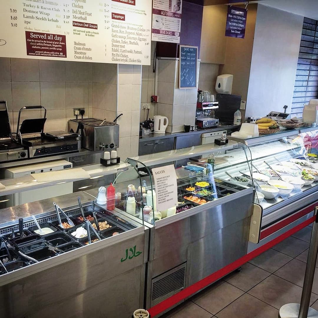 Bright deli counter showcasing a variety of fresh salads, wraps, and sauces, with a menu board above.