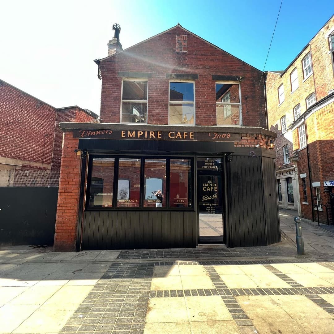 Charming brick facade of The Empire Cafe, featuring large windows and a welcoming entrance, set in a vibrant street.