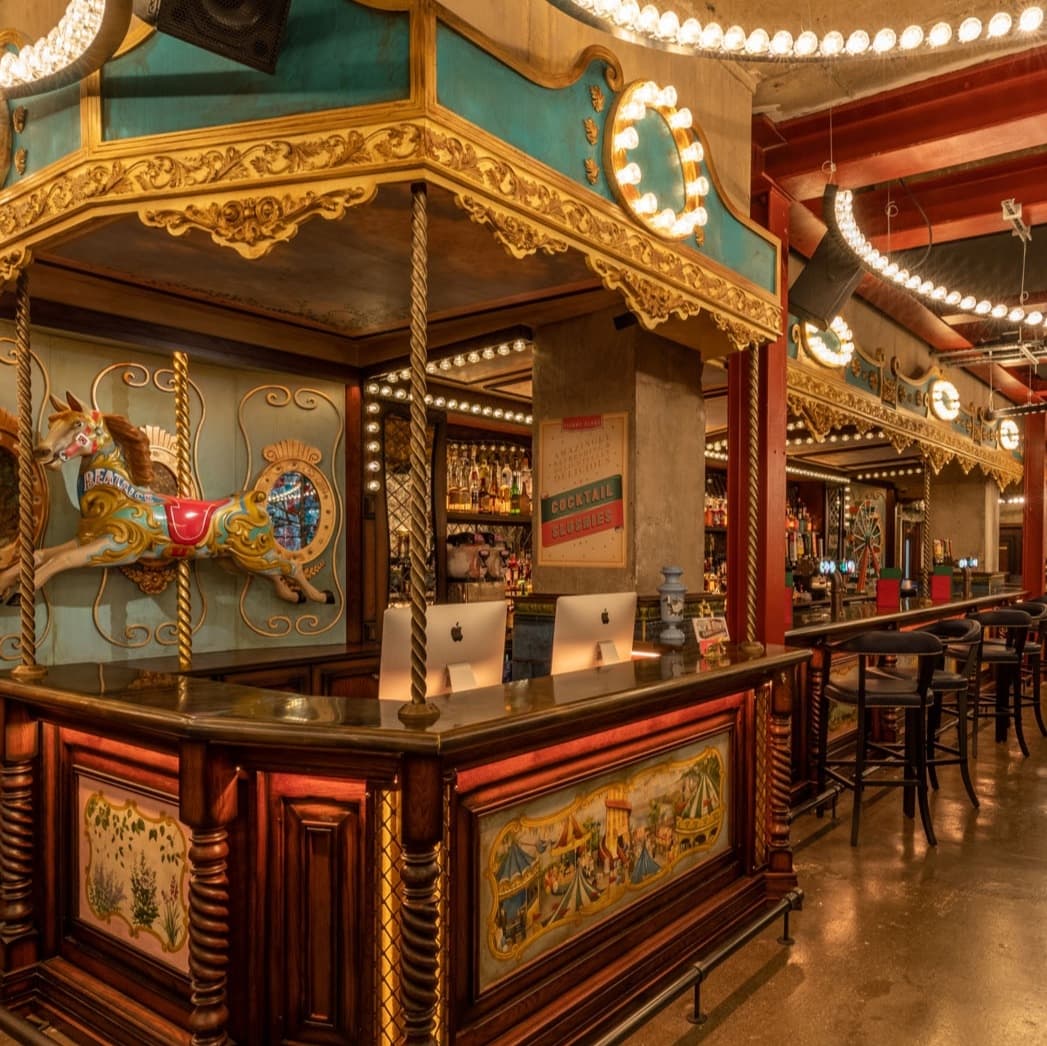 Colorful carousel-themed bar with ornate details, illuminated by warm lights, creating a vibrant, inviting atmosphere.