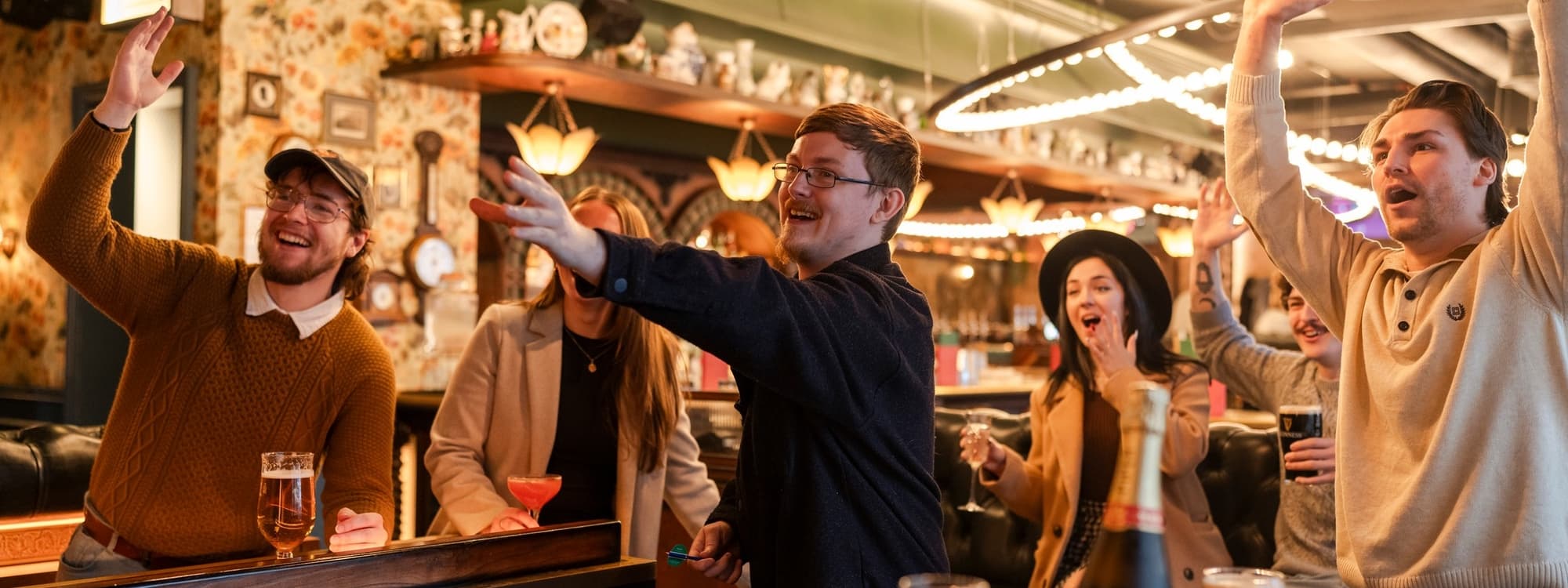 Group of excited friends celebrating at Flight Club Leeds, with drinks in hand and lively expressions.