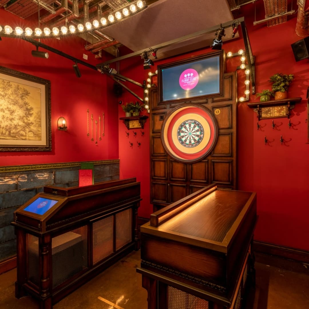 Cozy darts area with a wooden dartboard, red walls, soft lighting, and a digital scoreboard, inviting for social play.
